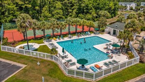 A large outdoor swimming pool surrounded by lounge chairs and umbrellas, with a tennis court and palm trees in the background. - Coral Hideaway: Balcony | Pool | Dog Friendly (Sunset Beach)