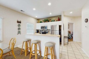 Une cuisine moderne avec des meubles blancs, des appareils en acier inoxydable et un coin bar équipé de tabourets.