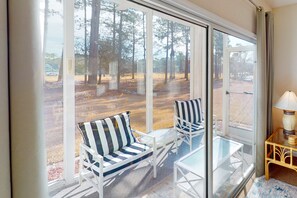 A room with a large sliding glass door leading to a covered outdoor area with chairs and a table. - Away on Avian #3406: Pool Access,Snowbird Friendly (Sunset Beach)