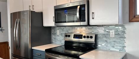 A modern kitchen with stainless steel appliances, a microwave, and a glass-tiled backsplash.