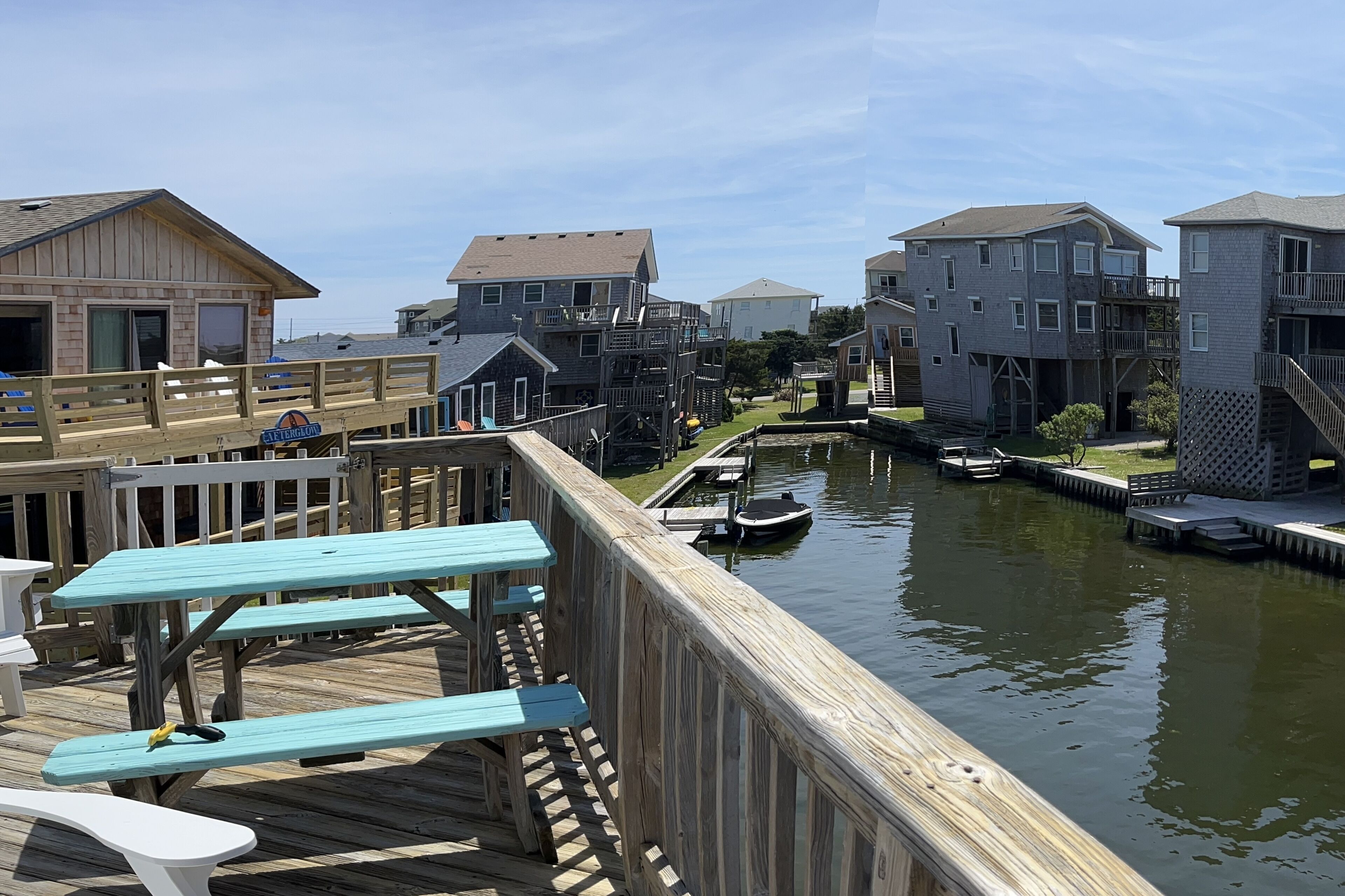 A wooden deck with picnic tables overlooking a canal with boats, surrounded by residential buildings.