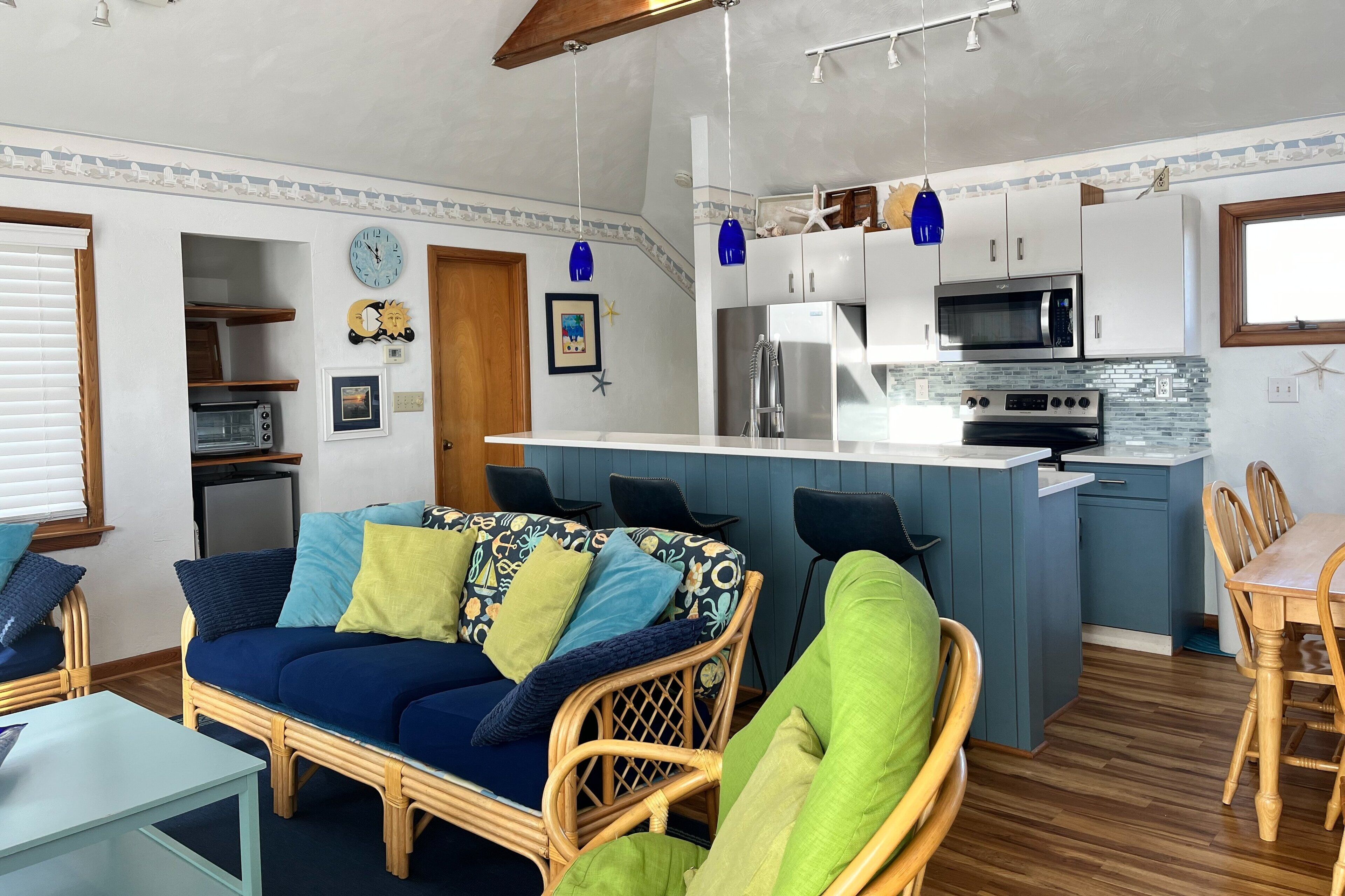 A compact living space with a kitchenette, a sofa with patterned cushions, a dining area, and a small table.