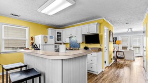 A kitchen with a central island, white cabinets, and a yellow accent wall. - Home near the beach with balconies, outdoor shower, grill, beach gear, W/D, & AC (Sunset Beach)
