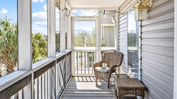 A covered porch with a ceiling fan, wicker furniture, and a view of the surrounding area. - Home near the beach with balconies, outdoor shower, grill, beach gear, W/D, & AC (Sunset Beach)