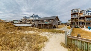 A beachfront property with a wooden deck, a sandy path, and multiple-story buildings with balconies. - Oceanfront, Dog-Friendly House w/ Free WiFi, Central AC, Private W/D, Ocean View (Hatteras)
