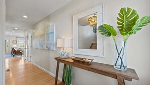Un couloir avec une console en bois, un miroir, une lampe et une grande plante.