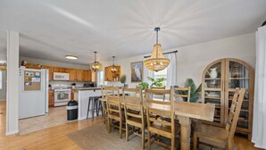 Une cuisine moderne avec des meubles en bois, une table à manger avec des chaises et un luminaire suspendu.