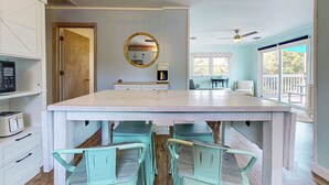 A spacious kitchen with a large island, white cabinets, and a round mirror. There are four green chairs around the island and a dining table. - Charming Family Getaway in Salvo with A/C, Full Kitchen, and Gas Grill (Salvo)