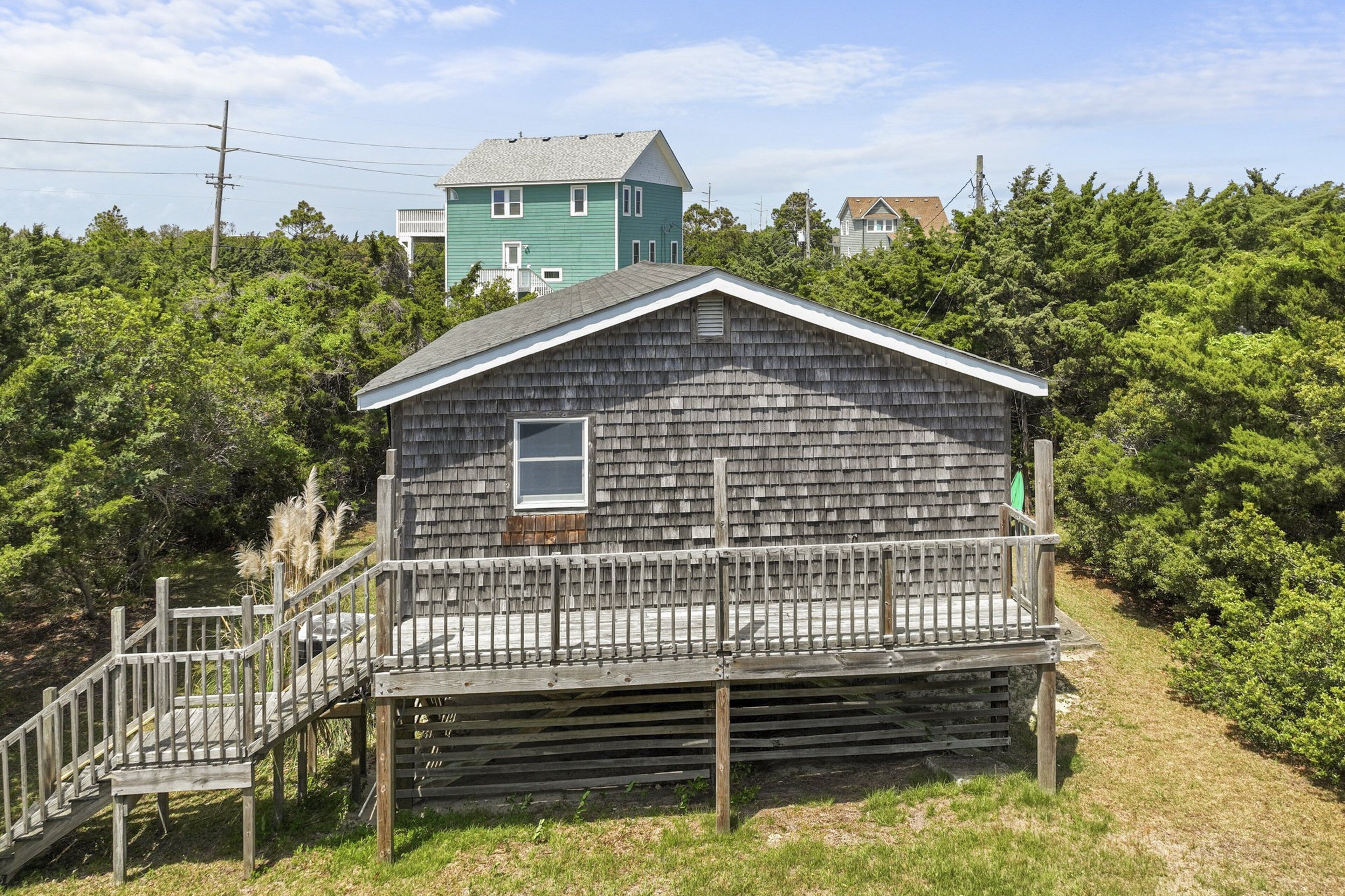 A wooden cabin with a porch and a small staircase leading up to it, surrounded by dense greenery.