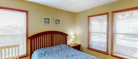 A bedroom with a bed, a chair, a nightstand, two wall-mounted pictures, and a ceiling fan.