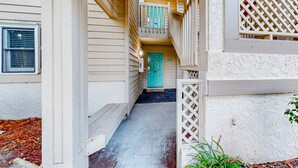 A narrow, covered walkway leading to a turquoise door, flanked by white lattice railings and wooden steps. - Ev's Escape,201A: Modern condo with sunroom - dog and snowbird-friendly (Sunset Beach)