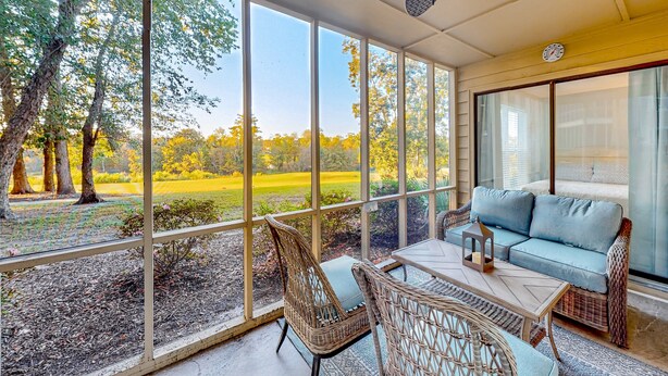A covered patio with wicker furniture, a blue sofa, and a view of a golf course. - Ev's Escape,201A: Modern condo with sunroom - dog and snowbird-friendly (Sunset Beach)