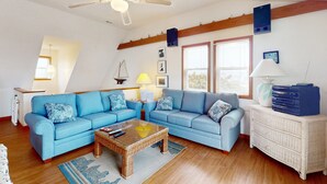 Ein Wohnzimmer mit zwei blauen Sofas, einem Couchtisch, einem Korbtisch, einem weißen Schrank und einem Deckenventilator.