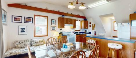 A spacious kitchen with wooden cabinets, a central island with stools, and a dining table with chairs.
