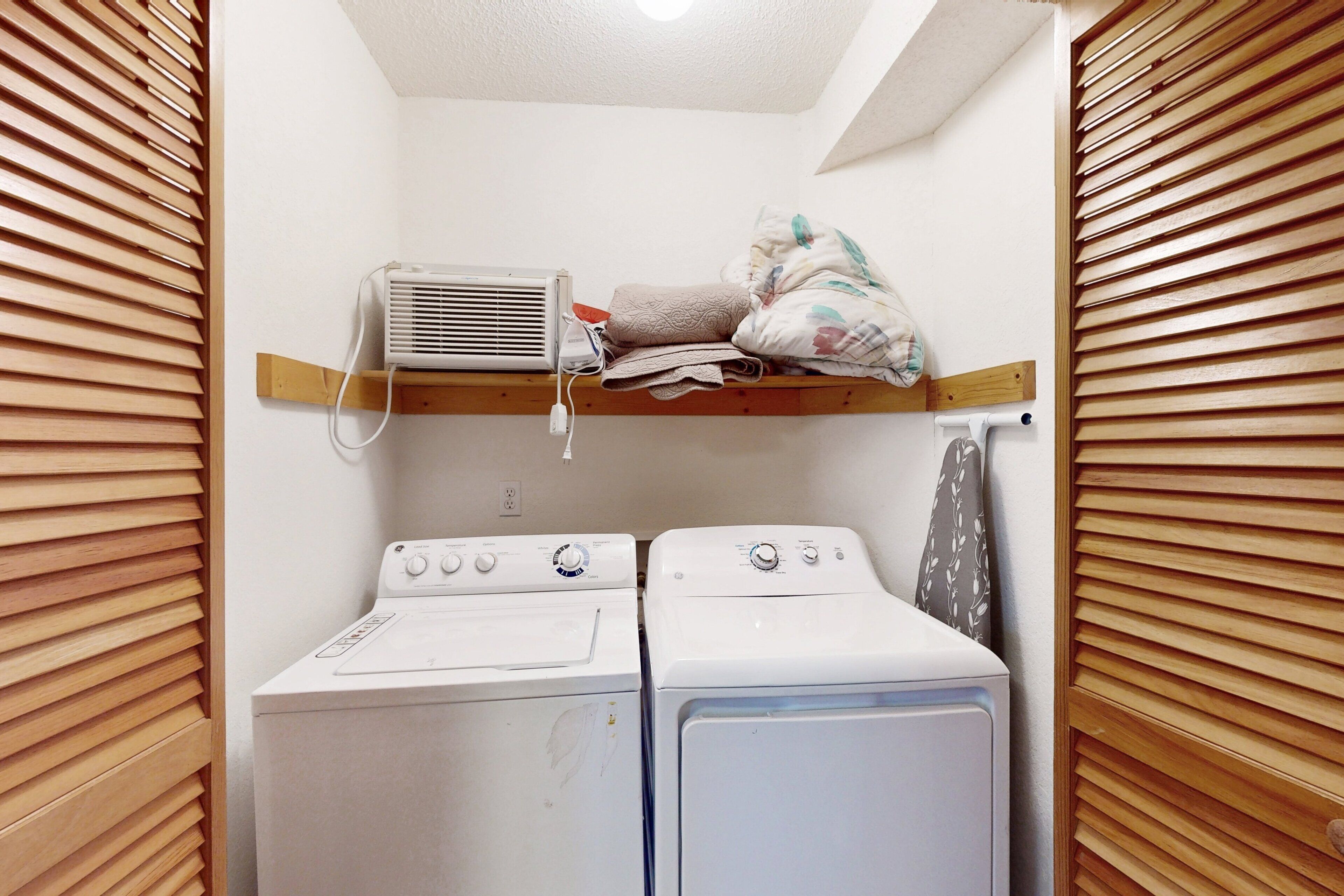 Un cuarto de lavandería con lavadora y secadora, paredes con listones de madera y un respiradero en el techo.