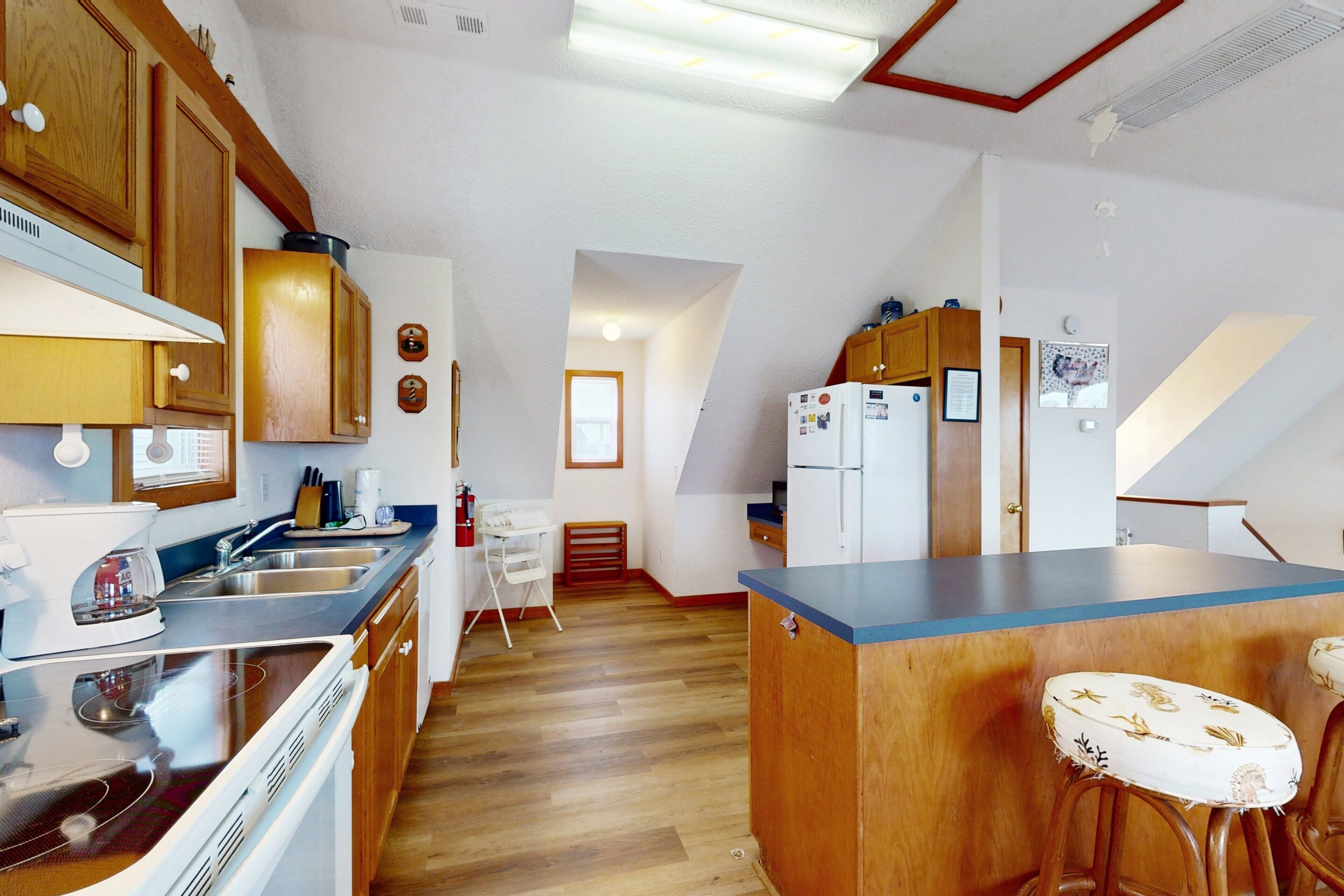 Eine kompakte Küche mit Holzausstattung, einem eingebauten Herd, einem Kühlschrank und einer kleinen Essecke mit einem Hocker.