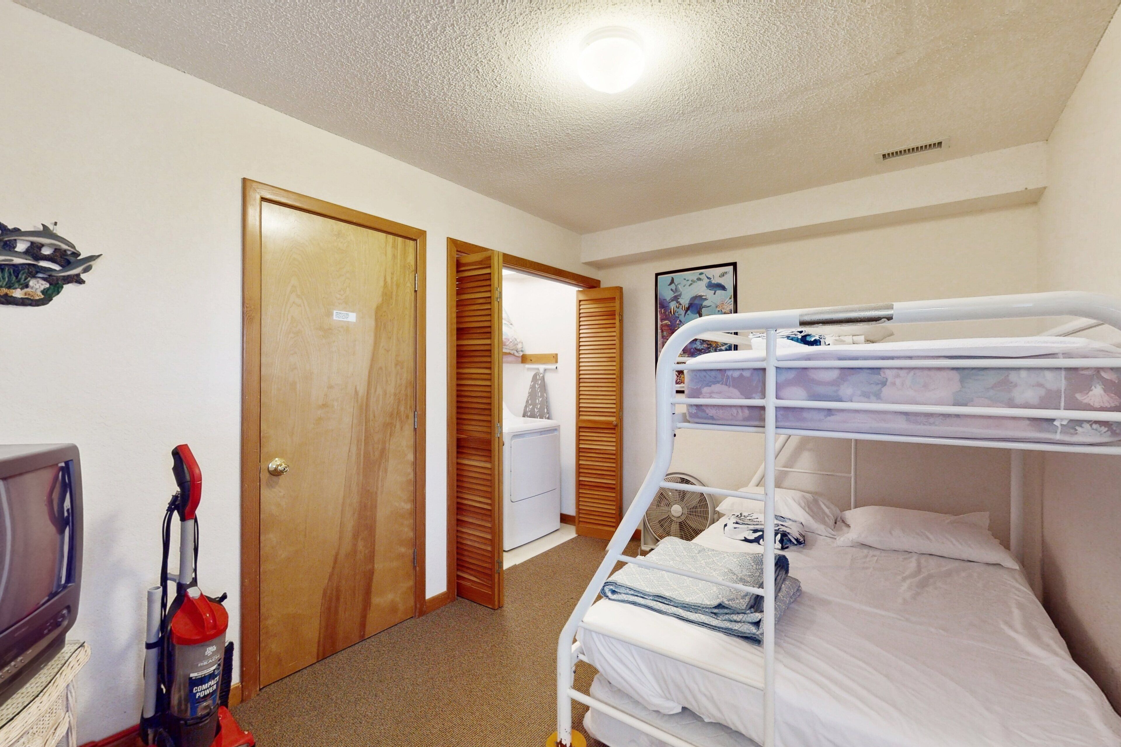 Una habitación con literas, una puerta, un aspirador y un televisor.
