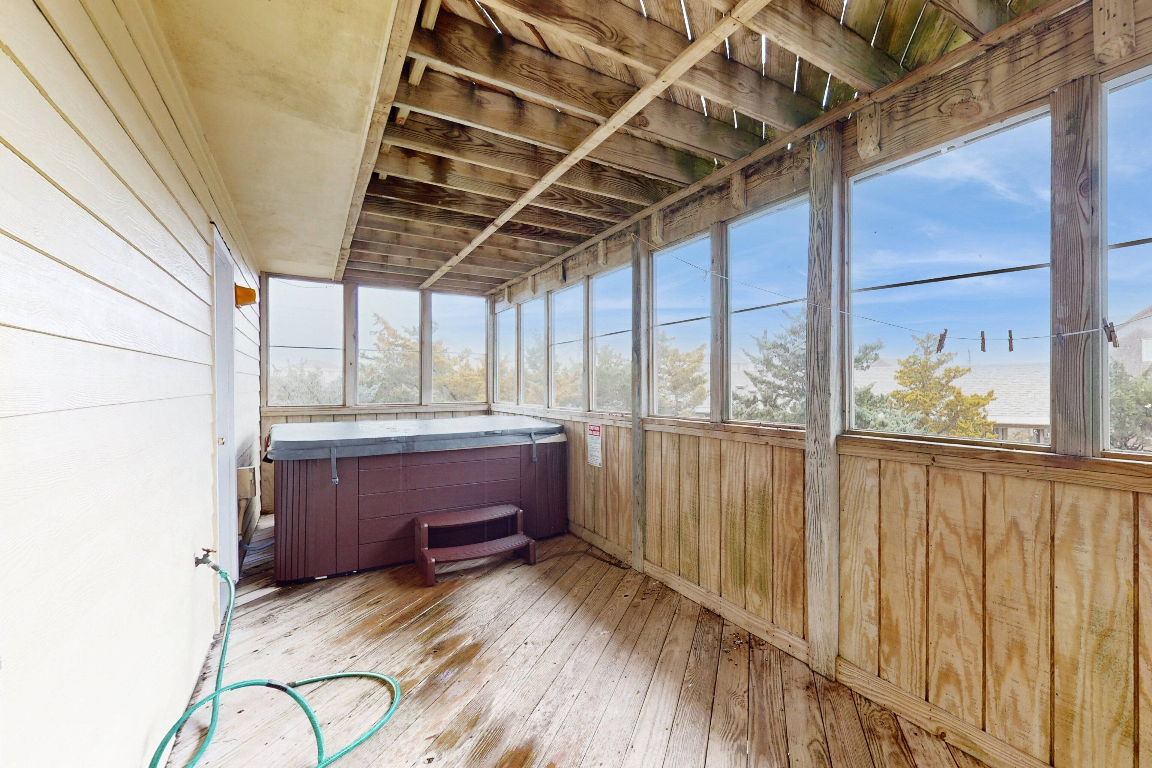Un espacio al aire libre cubierto con paredes de madera y ventanas amplias, un jacuzzi y una manguera en el suelo.