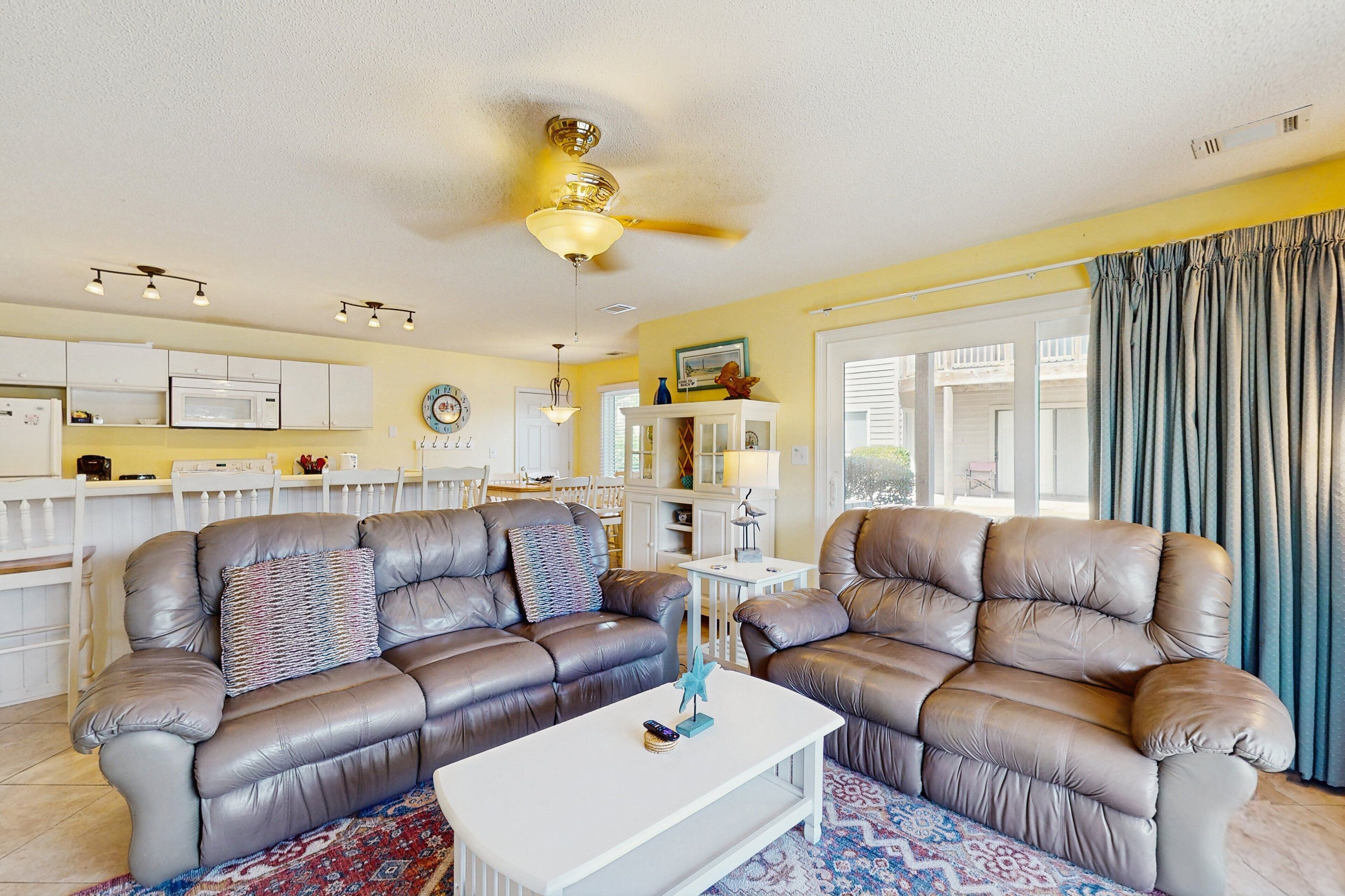 A living room with two leather sofas, a white coffee table, and a ceiling fan.