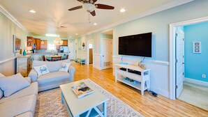 A spacious living room with a ceiling fan, a television, and a dining area in the background. - Open, beautiful ocean-view home with pool, hot tub & lanai - snowbird-friendly (Rodanthe)