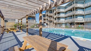 A poolside area with wooden pergolas, picnic tables, and a pool. - Open, beautiful ocean-view home with pool, hot tub & lanai - snowbird-friendly (Rodanthe)
