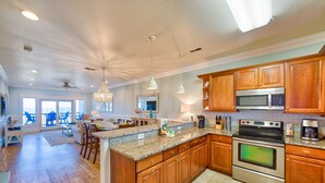 A spacious kitchen with wooden cabinets, stainless steel appliances, and a large island with bar stools. - Open, beautiful ocean-view home with pool, hot tub & lanai - snowbird-friendly (Rodanthe)