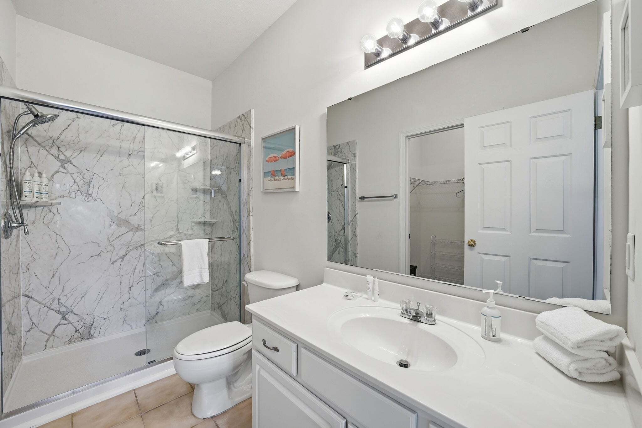 Une salle de bain moderne avec une douche à parois de verre, des toilettes blanches, un meuble-lavabo et un grand miroir.