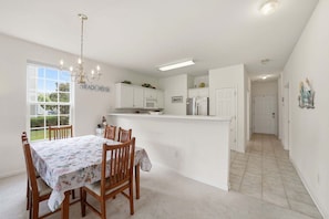 Una cocina con armarios blancos, un comedor con mesa y sillas, y un cartel que dice 'BEACH HOUSE'.