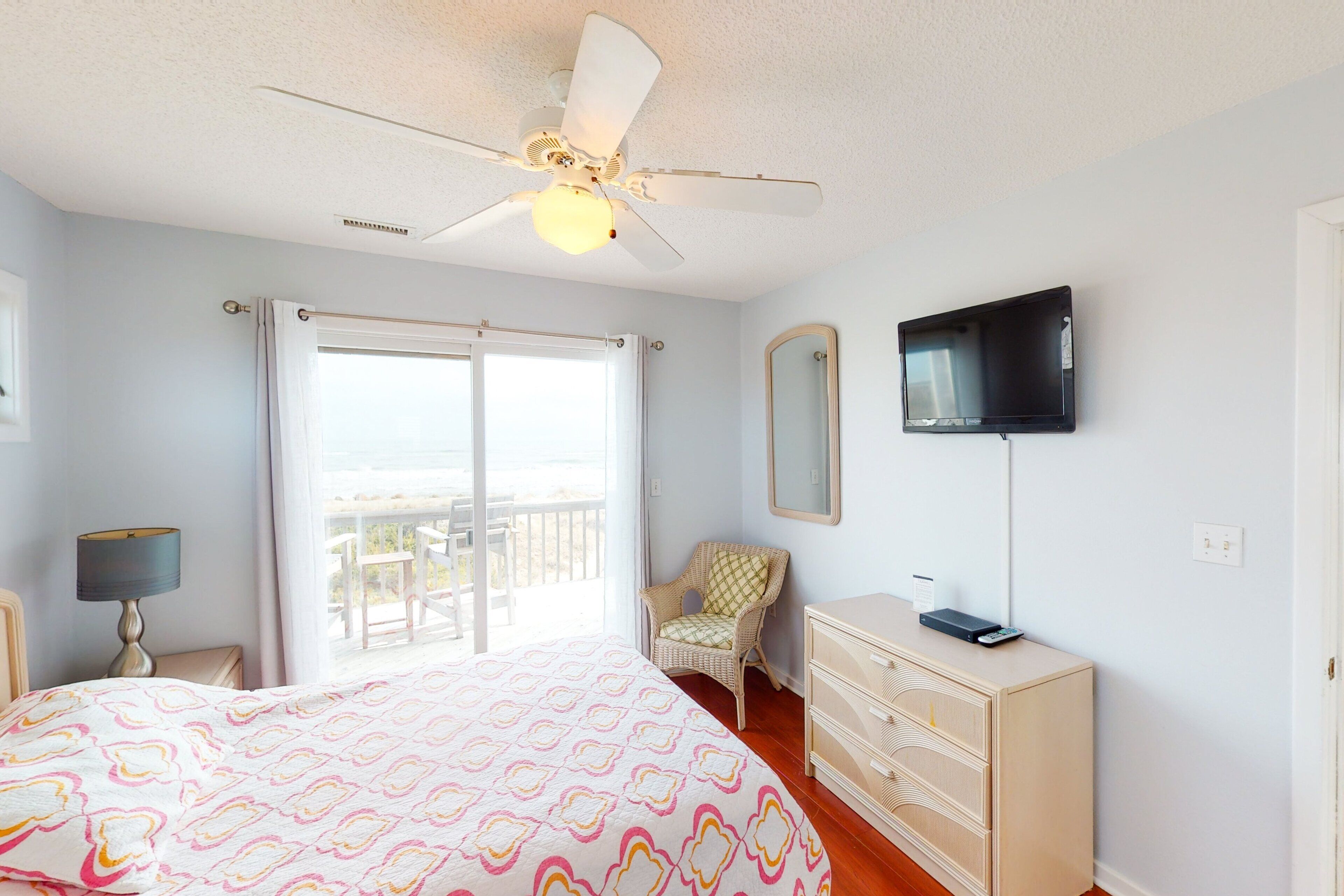 A bedroom with a bed, a ceiling fan, a television, a chair, and a dresser.