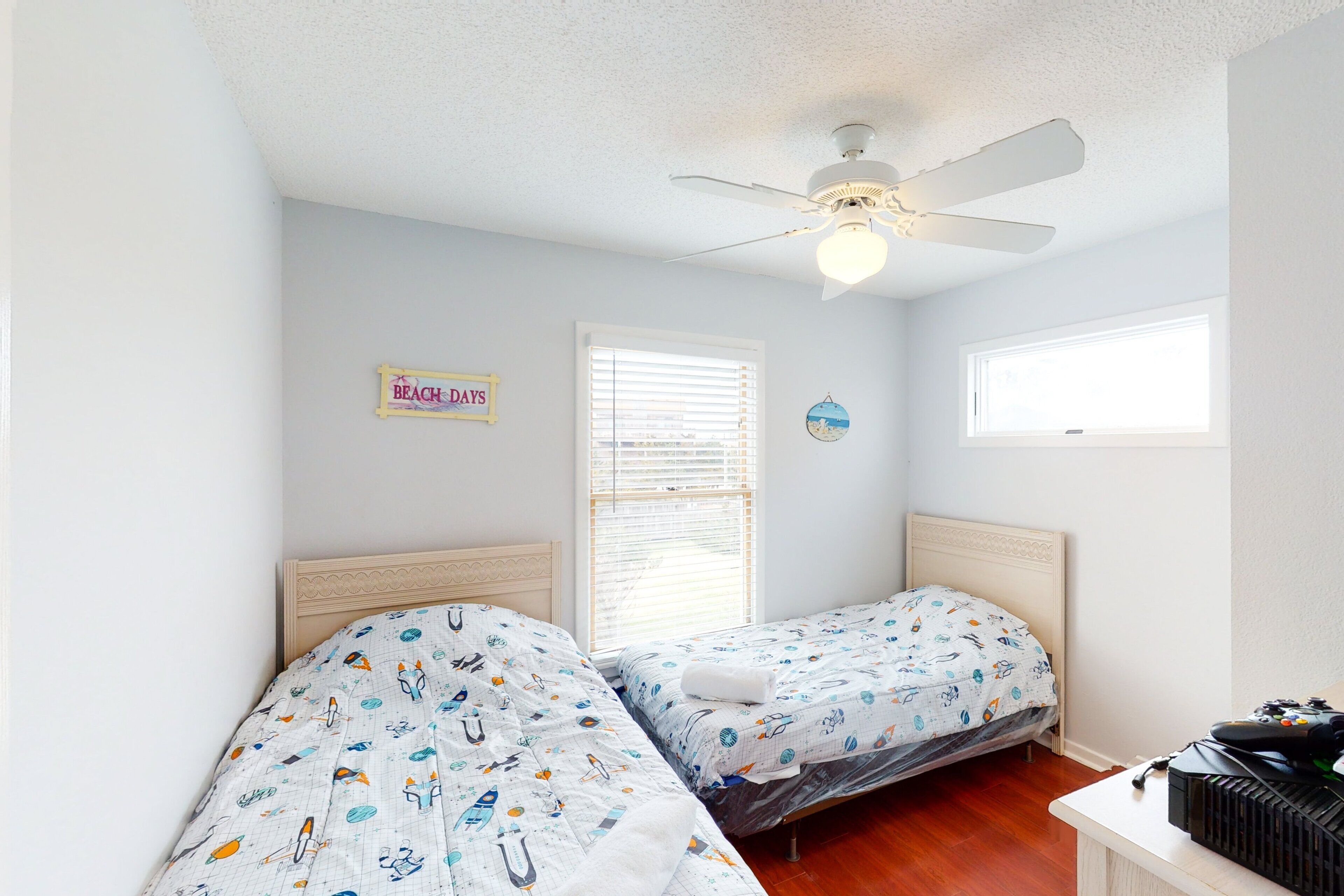 A bedroom with two beds, a ceiling fan, a window with blinds, and a sign on the wall.
