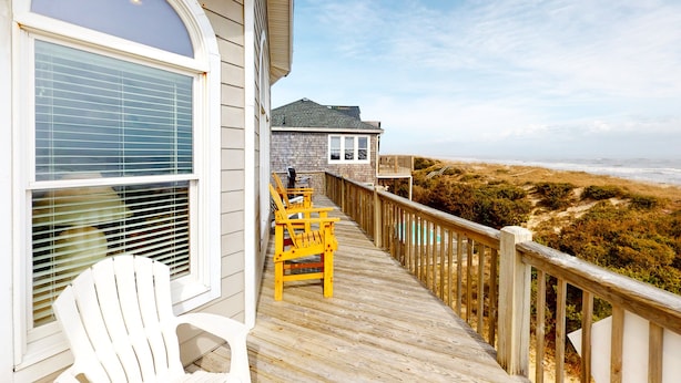 A wooden deck with a railing, a white chair, and a table with yellow chairs. - Oceanfront home with incredible beach views, washer/dryer & pool (Avon)