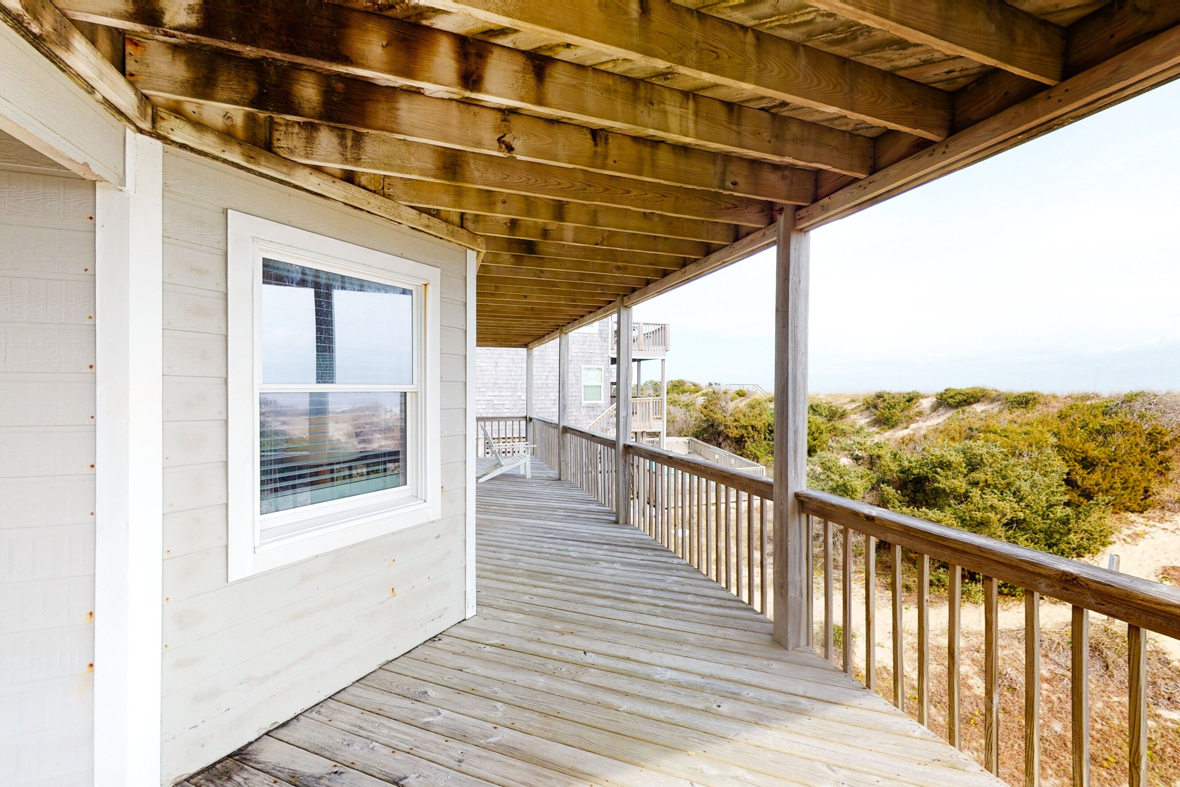 A wooden deck with a railing, a window, and a view of the landscape.