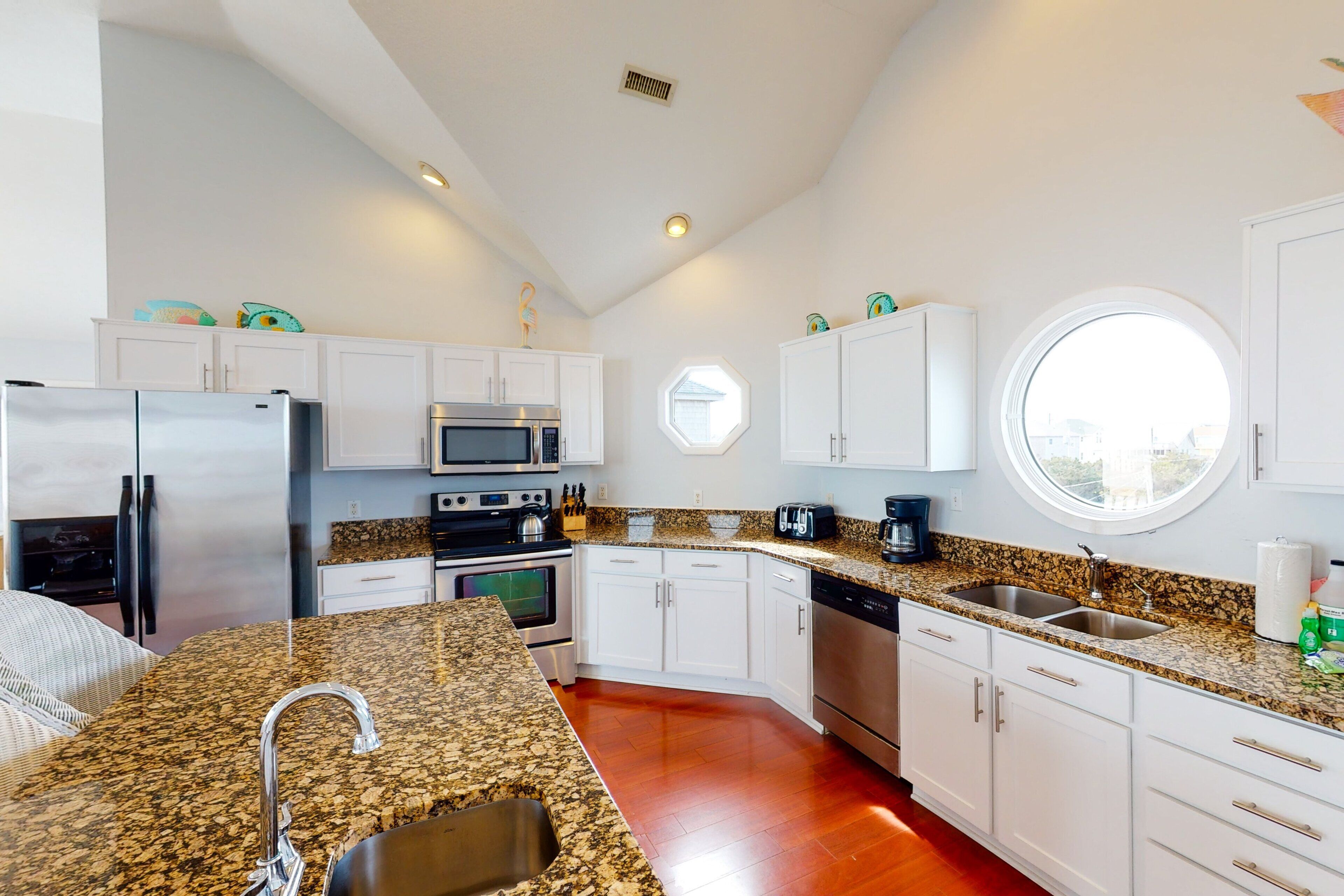 A modern kitchen with white cabinets, granite countertops, stainless steel appliances, and a large window.