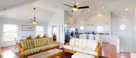 A spacious living area with a high ceiling, a dining table, and a kitchen in the background.