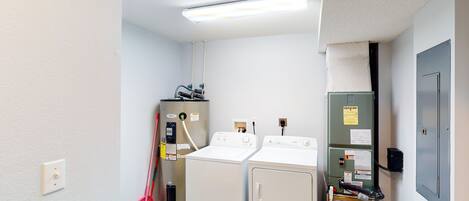 Une buanderie équipée de deux machines à laver, d’un sèche-linge et d’un compteur d’eau.