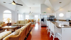 A spacious living area with a large sofa, a dining table, and a kitchen with white cabinets and a granite countertop. - Oceanfront home with incredible beach views, washer/dryer & pool (Avon)