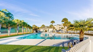 Ein Swimmingpool mit weißem Deck, umgeben von Palmen und einem Zaun.