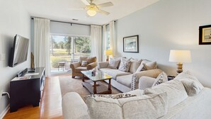 Ein Wohnzimmer mit einer Sofagarnitur, einem Couchtisch, einem Fernseher und einem Deckenventilator.