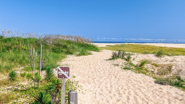 Ein Sandweg am Strand, der zum Meer führt, mit einem Schild, das auf einen Aussichtspunkt hinweist.