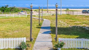 Ein hölzerner Weg führt zum Strand, gesäumt von weißen Zäunen und Laternen.