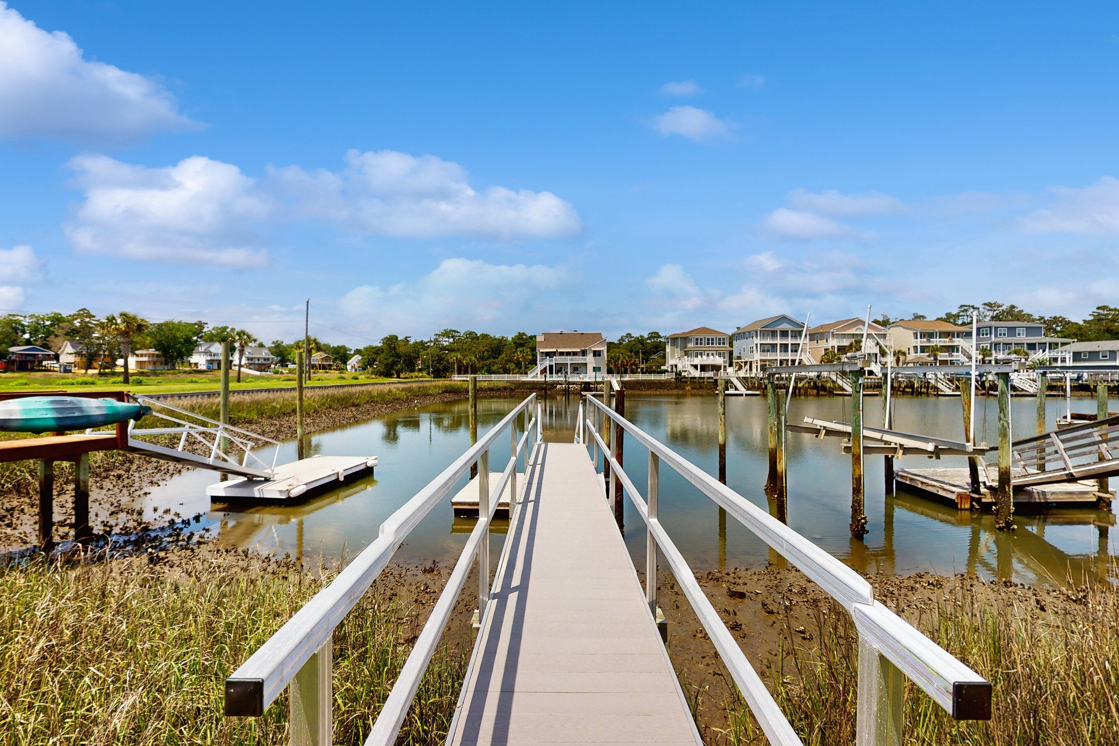 A wooden boardwalk leading to a marina with houses in the background.