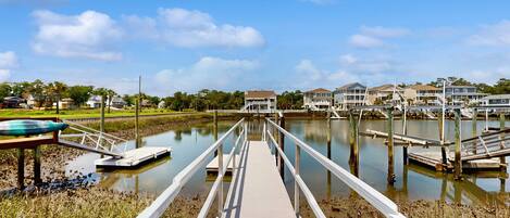A wooden boardwalk leading to a marina with houses in the background.