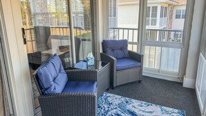 A balcony with wicker furniture, a glass table, and a view of neighboring houses. - SB72A&B: Coastal Condo with golf course view and shared pool access (Sunset Beach)