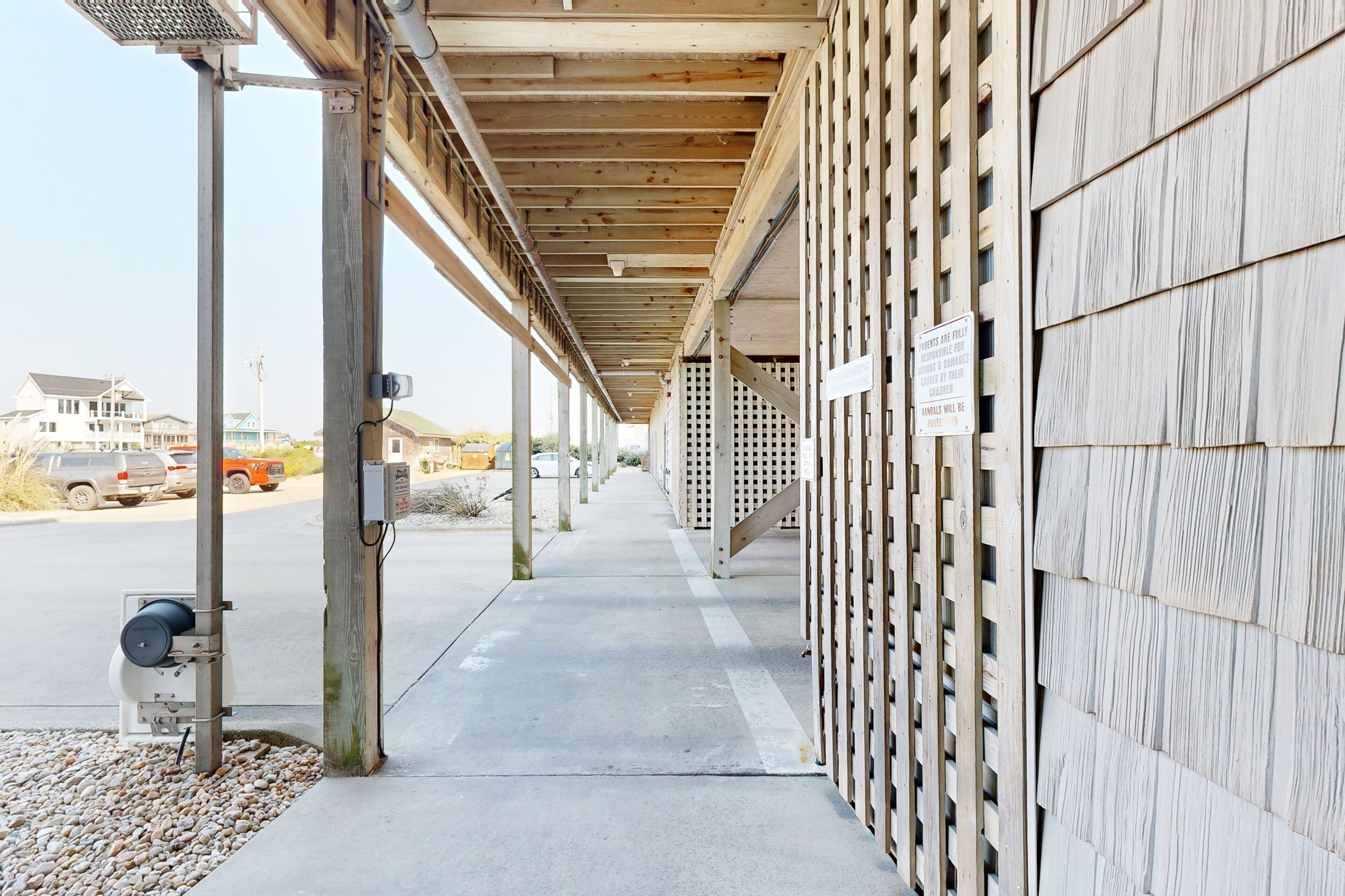 A covered outdoor area with a concrete walkway, wooden beams, and a sign indicating a private parking area.