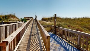 A wooden boardwalk leading to a beach area with a clear sky. - Inviting beachfront condo featuring hot tub & pool, central AC, elevator, & deck (Hatteras)
