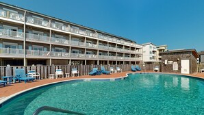 A multi-story hotel with a swimming pool, outdoor seating, and a wooden fence. - Inviting beachfront condo featuring hot tub & pool, central AC, elevator, & deck (Hatteras)