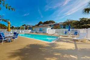Ein Poolbereich mit einem Schwimmbecken von 2,7 mal 3,6 Metern, umgeben von weißen Zäunen, blauen und weißen Liegestühlen und einem gelben Sonnenschirm.