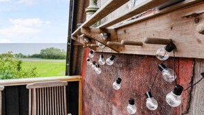 A rustic wooden balcony with a view of a green field and a body of water. - 5 Star Holiday Home in Svaneke (Svaneke)