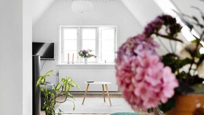 A modern living room with a large window, a flat-screen TV, a small round table, and various plants. - 5 Star Holiday Home in Svaneke (Svaneke)
