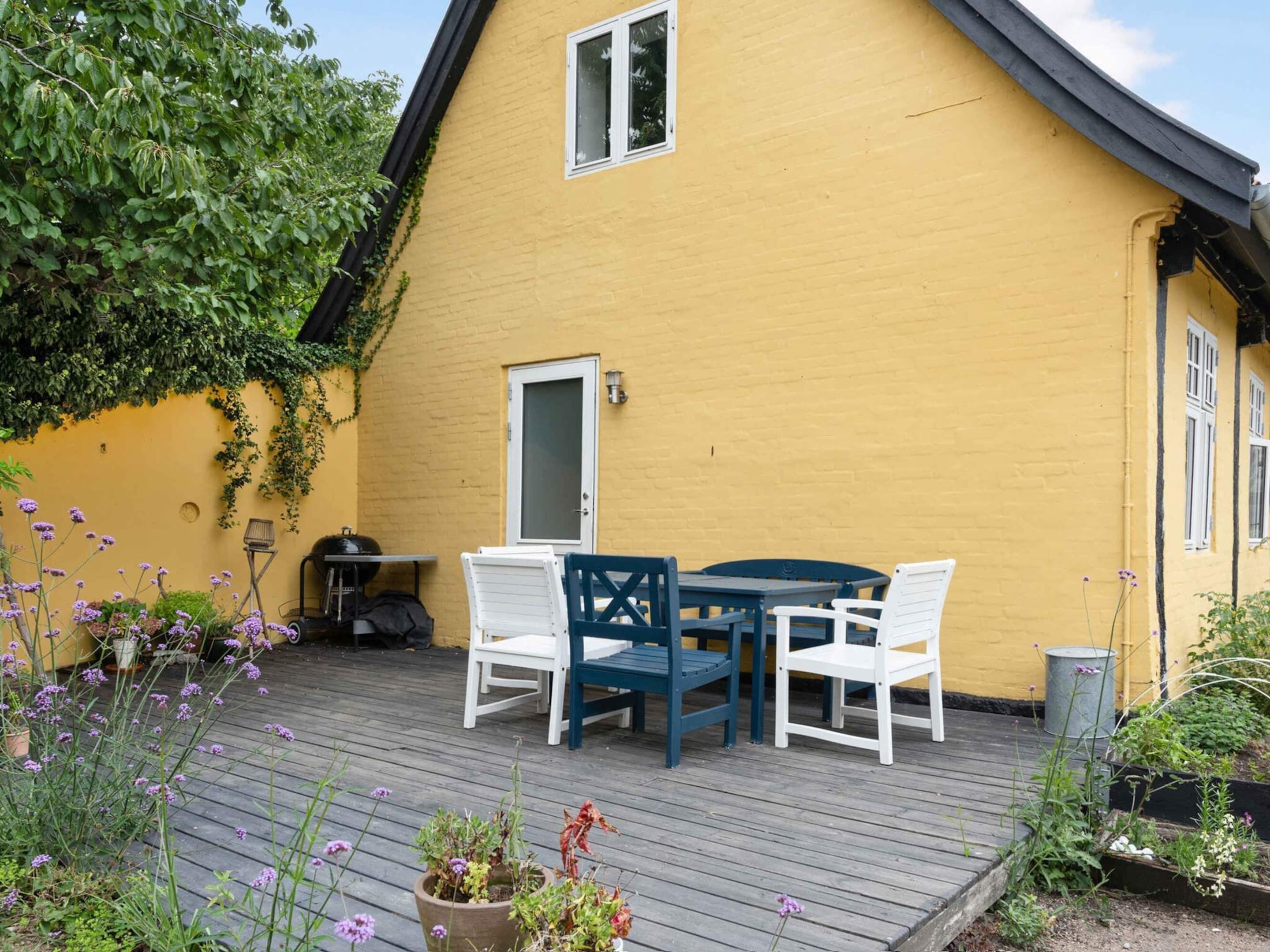 A yellow house with a deck, white chairs, and a table.